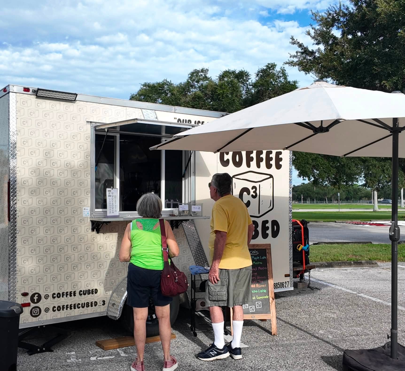 A couple ordering at the cream-colored Coffee Cubed trailer under a wide umbrella