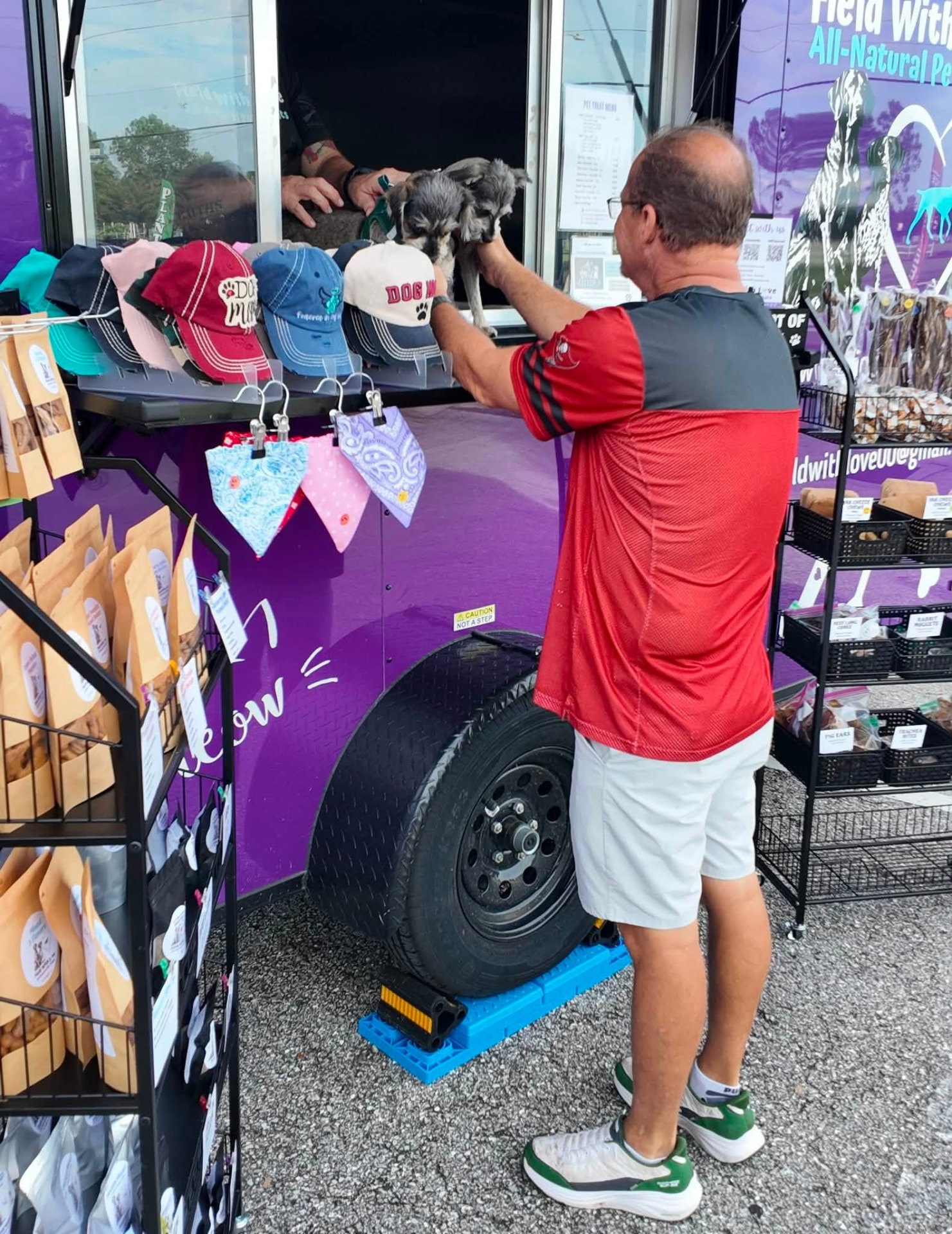 A little dog being lifted up to the pet treat trailer window for a snack