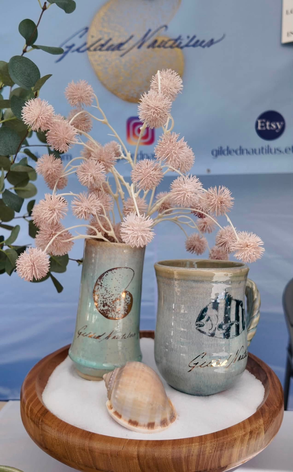 Two glazed handmade mugs holding dried pink blooms on a wooden tray