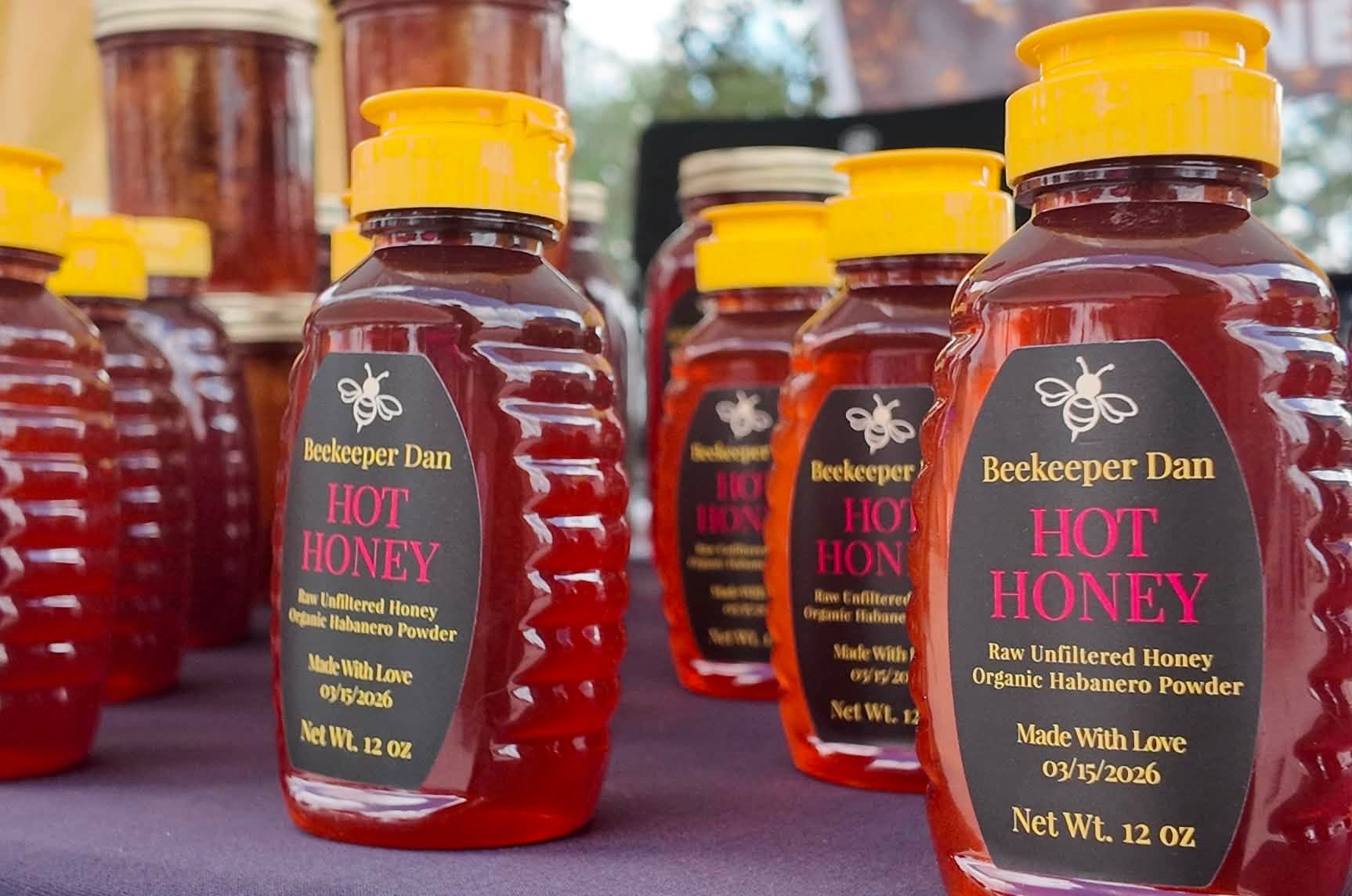 Rows of Beekeeper Dan hot honey bottles glowing amber in the sun