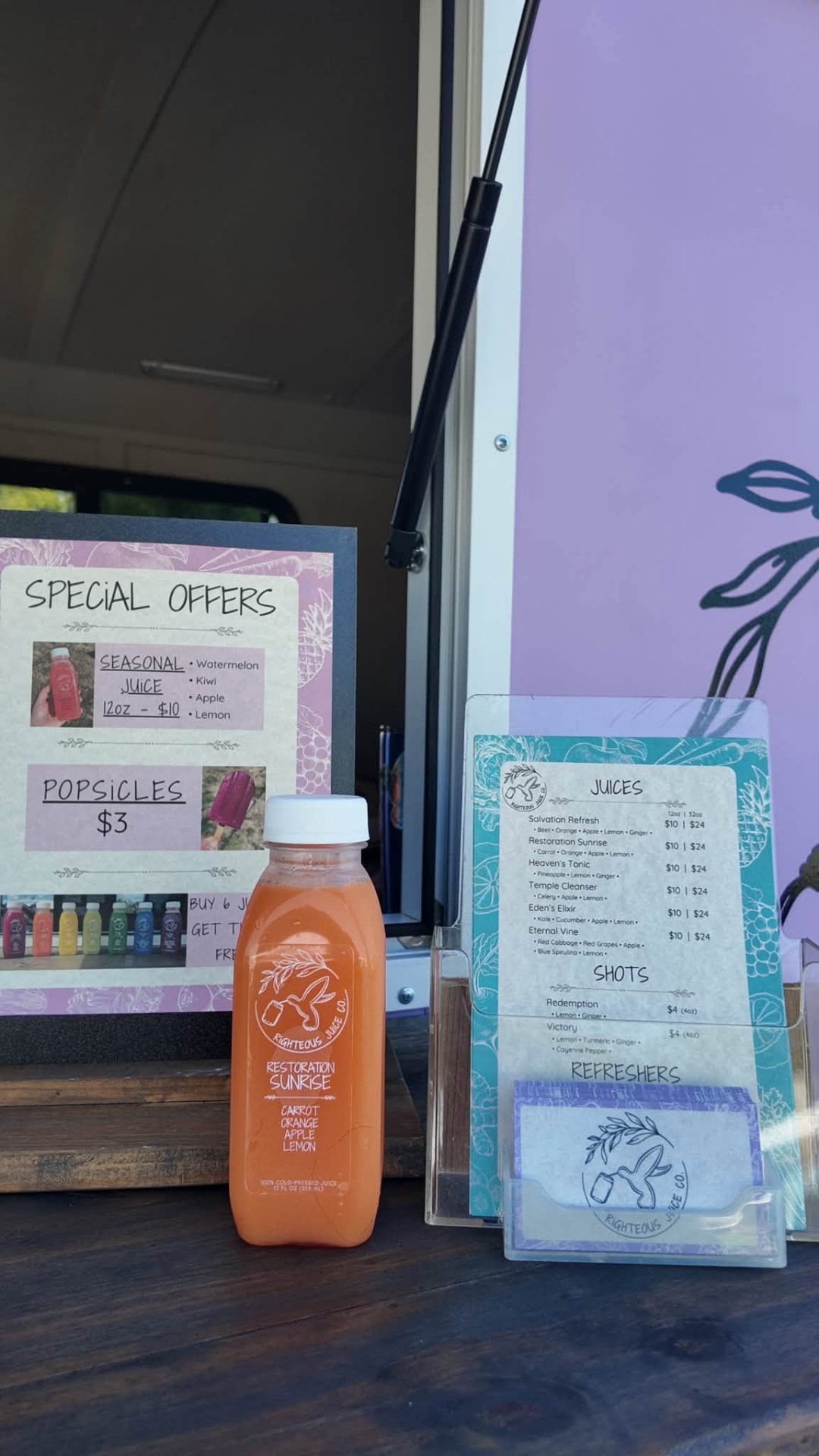 A bottle of cold-pressed carrot and orange juice beside a hand-lettered juice menu