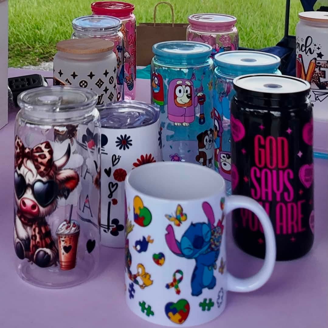 A cheerful lineup of hand-decorated glass tumblers and mugs on a lavender table