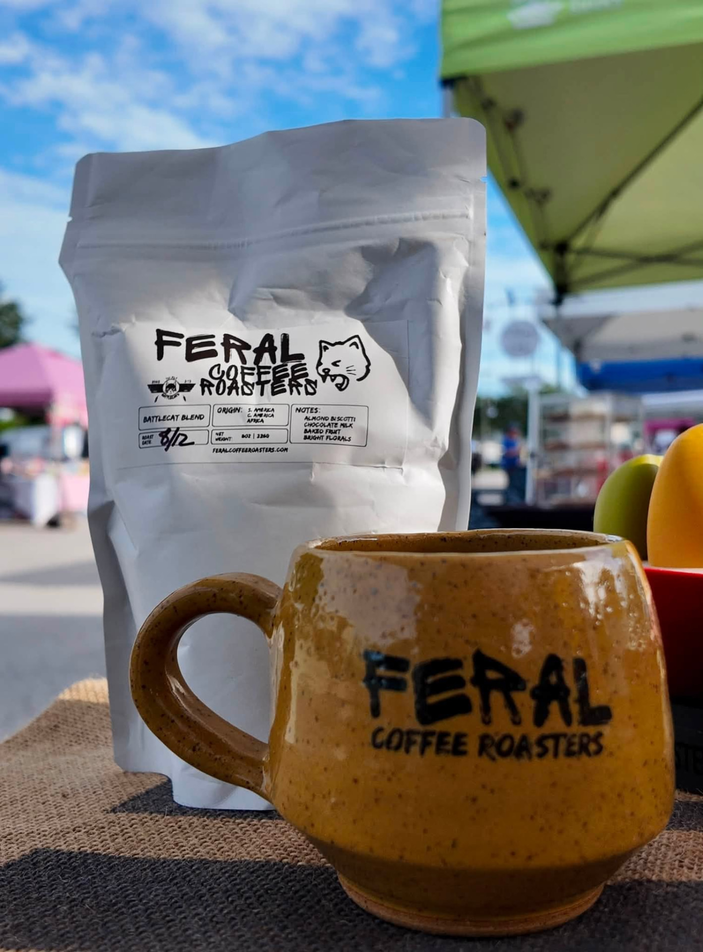 A bag of Battlecat Blend coffee next to a hand-thrown speckled mug on burlap