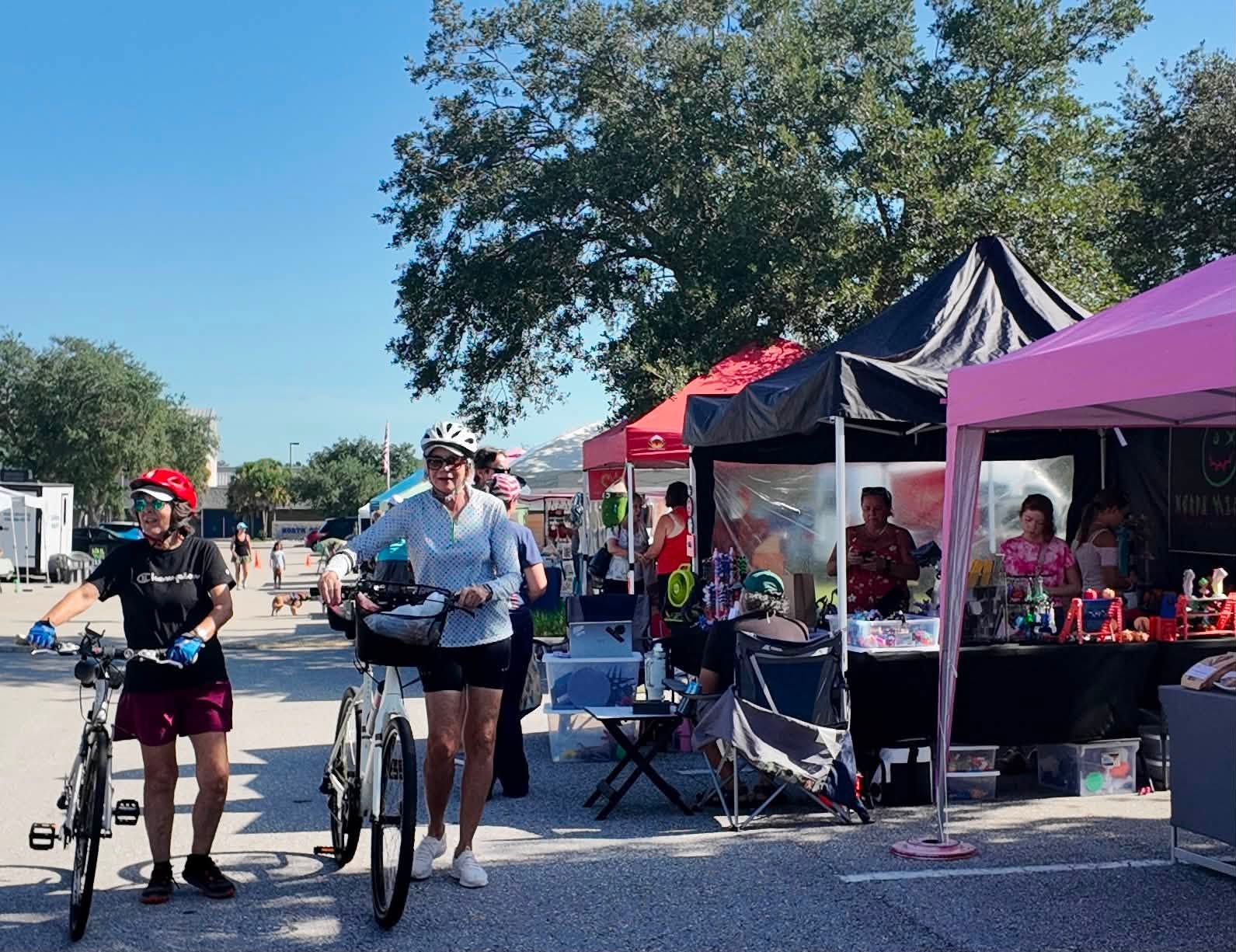 Two cyclists pausing at the market with their bikes beside a pink vendor tent