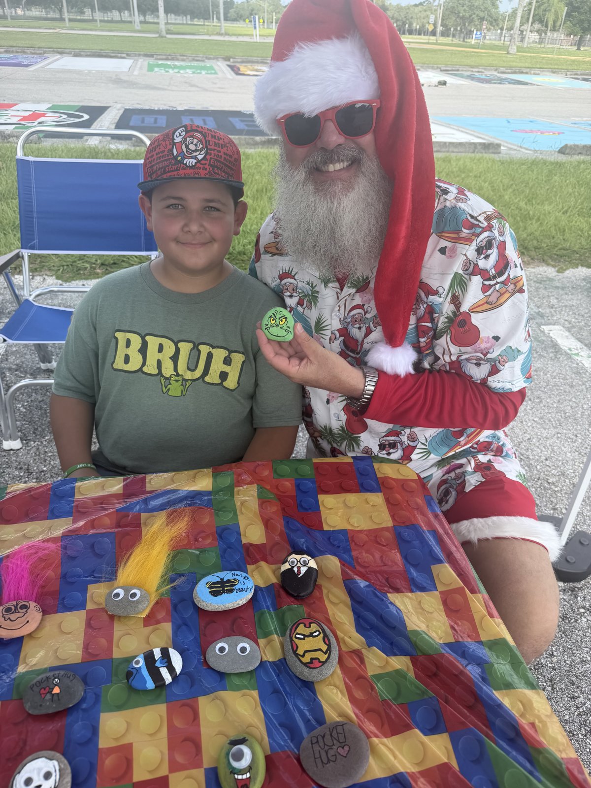A young Biz Kidz maker showing off his hand-painted pocket hug rocks with beach Santa at his table