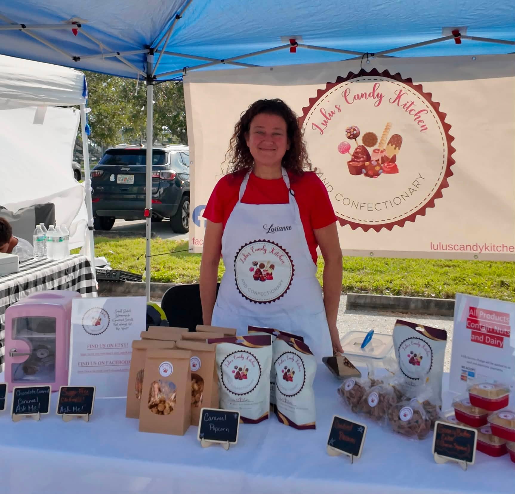 A candy maker smiling behind her table of caramels, popcorn and chocolate treats